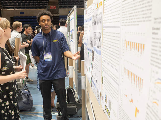 An undergraduate student explains his research findings to a faculty moderator at the 2023 research conference poster session.