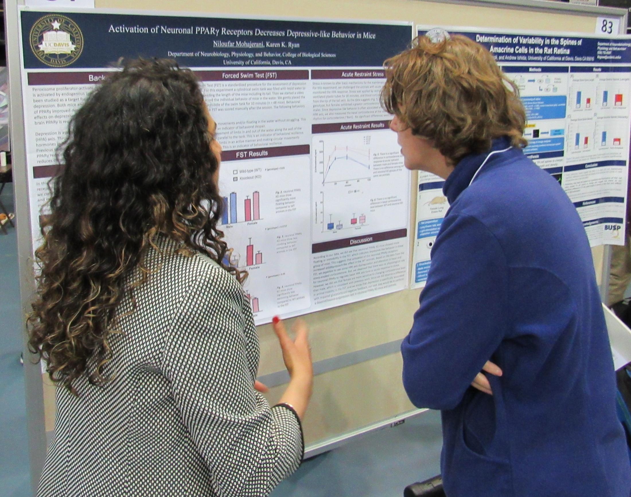 A student is presenting her research poster to a faculty moderator who is looking closely at the poster