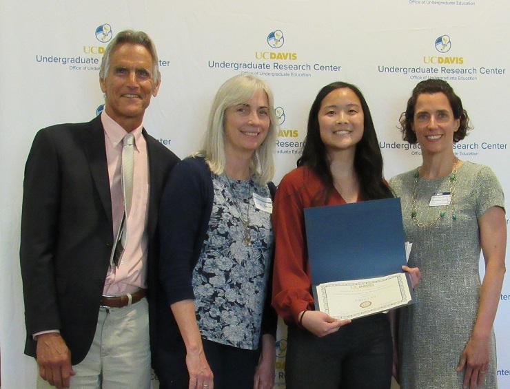 Photo of Steve and Karen Hanson, Aileen Lam holding her certificate and Annaliese Franz in front of a URC photo back drop