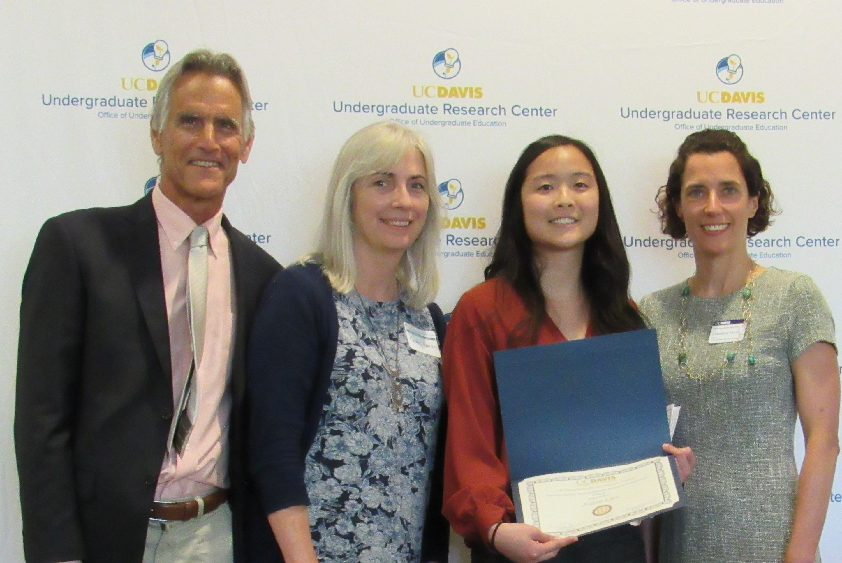 Photo of Steve and Karen Hanson and Annaliese Franz standing with Publication Award Recipient in front of backdrop with URC logos