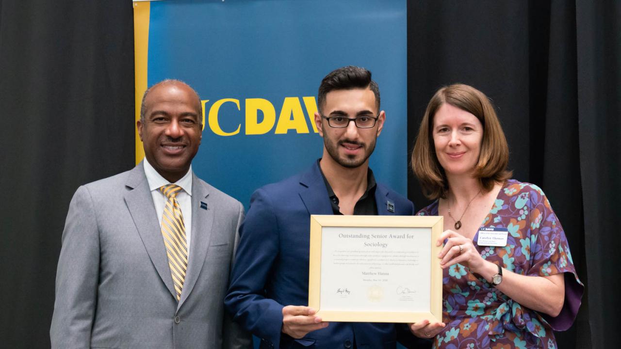 Photo of Mark Hanna, Mentor Mentee student alumnus accepting an award with Chancellor May on the left and Dean Carolyn Thomas on the right