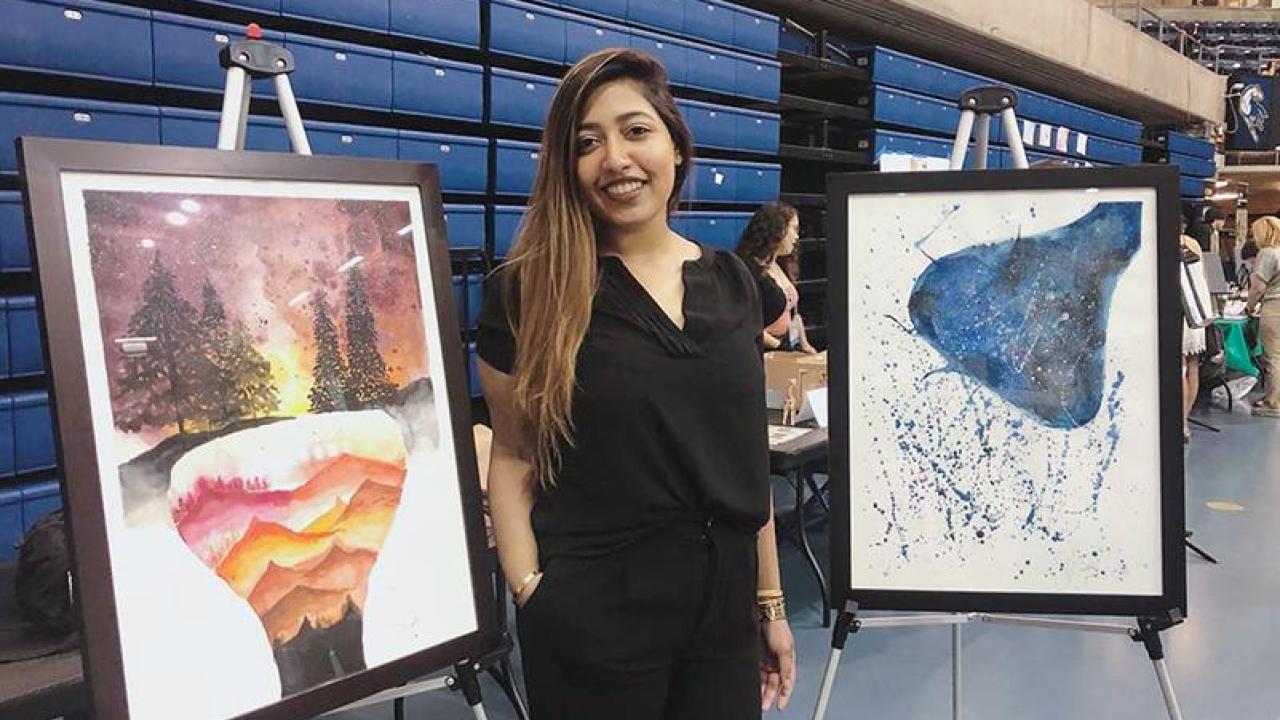 The Art of Harm Reduction is a three-part watercolor series by Sid Ganesh that attempts to "embody the lived experiences of persons who use drugs." Photo of Sid Ganesh standing with two watercolor paintings at the Undergraduate Research Conference