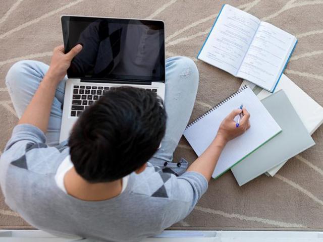 Student studying on floor with laptop and papers