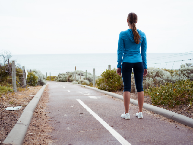 A photo of a jogger standing on a paved pathway looking into the distance