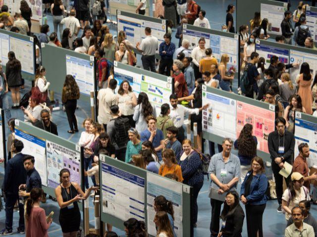 An overhead photo of the URSCA 2023 Conference Poster session showing multiple presenters in front of posters on poster boards and multiple attendees