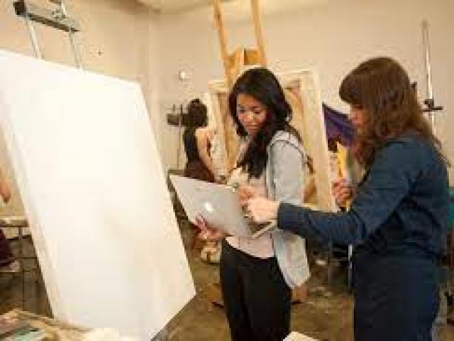 A faculty mentor guiding a student in art studio beside a large canvas