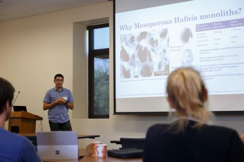 CAMP Student standing in front of seated audience giving a presentation of slide show shown on large screen next to student presenter