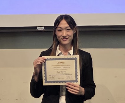 Smiling young woman in dark blazer holding certificate on stage (photo)
