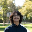 Outdoor portrait of young man with curly hair, glasses and dark shirt in sunny park